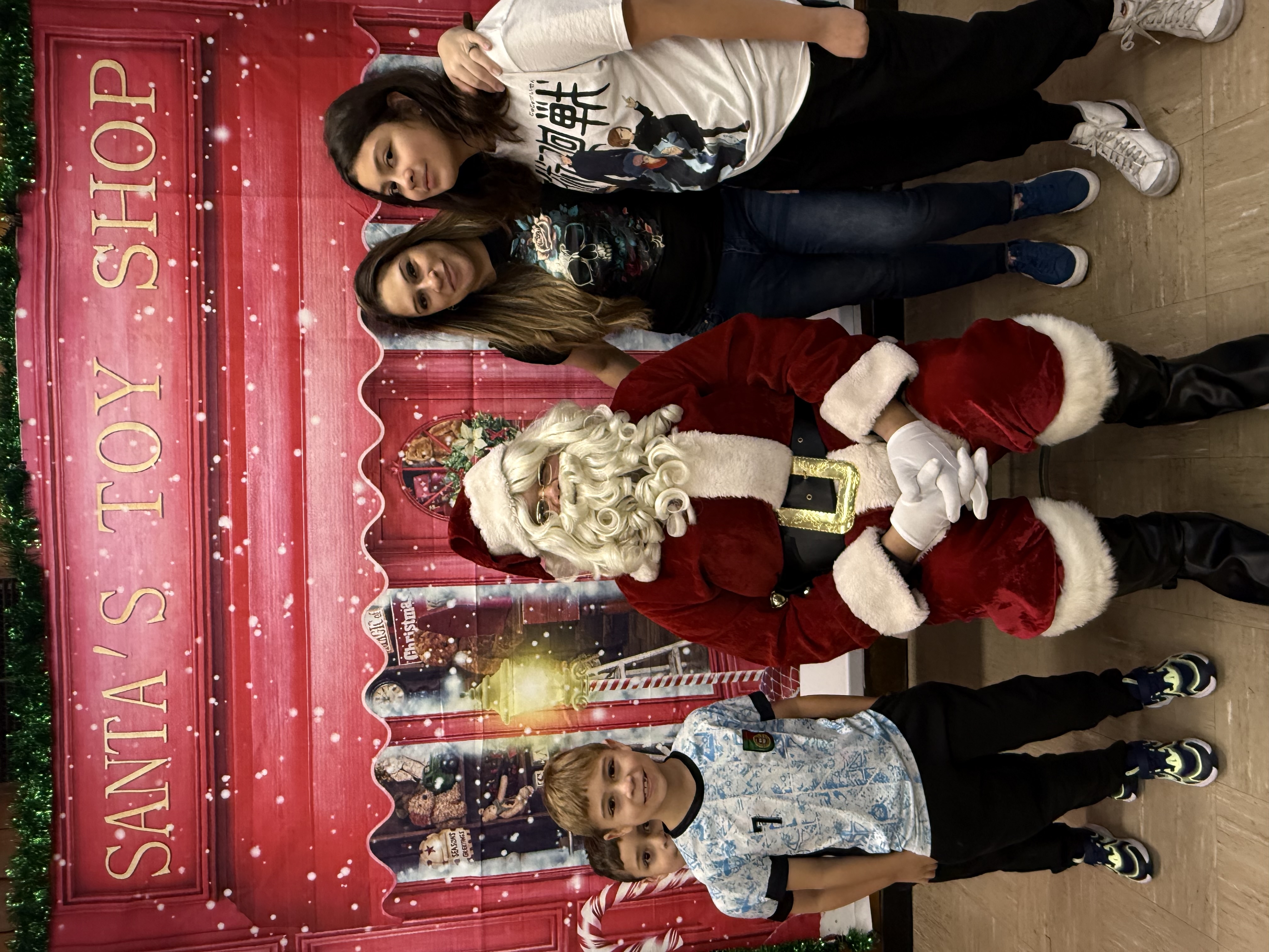 Santa with two girls and two boys in front of a toy shop backdrop.